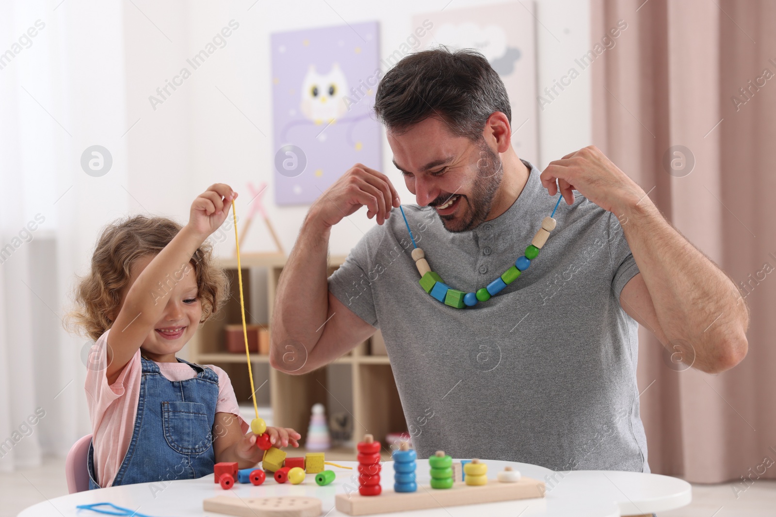 Photo of Motor skills development. Father and daughter playing with wooden pieces and string for threading activity at table indoors