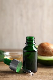Photo of Bottle of essential oil, pipette and fresh avocado on wooden table