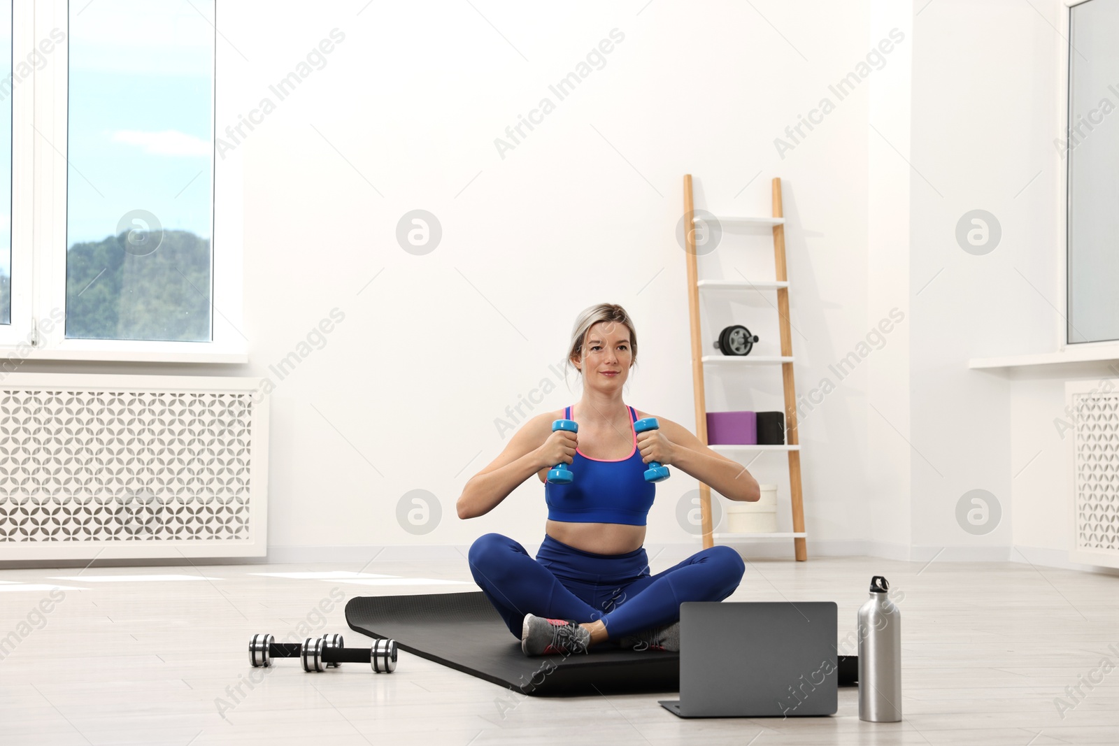 Photo of Online fitness trainer. Woman doing exercise with dumbbells near laptop at home