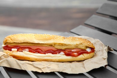 Photo of Fresh delicious hot dog with sauce on black bench outdoors