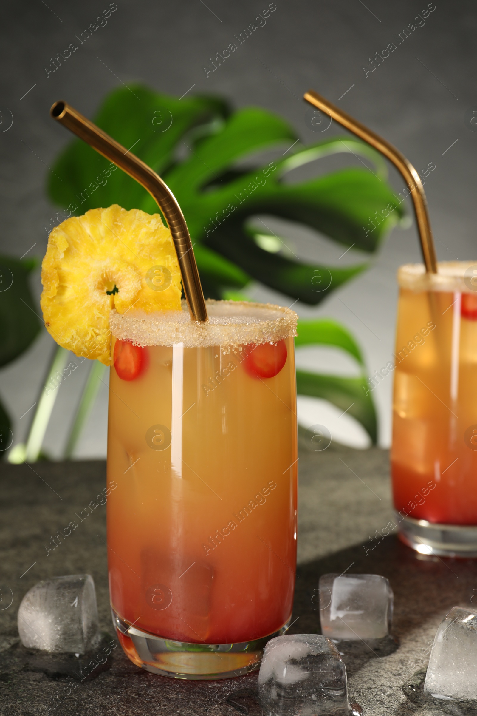 Photo of Glasses of tasty pineapple cocktail and ice cubes on grey table