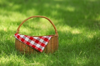 Photo of Wicker basket with blanket on green grass in park, space for text. Summer picnic