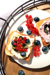 Photo of Sandwiches with cream cheese and berries on wooden tray, flat lay