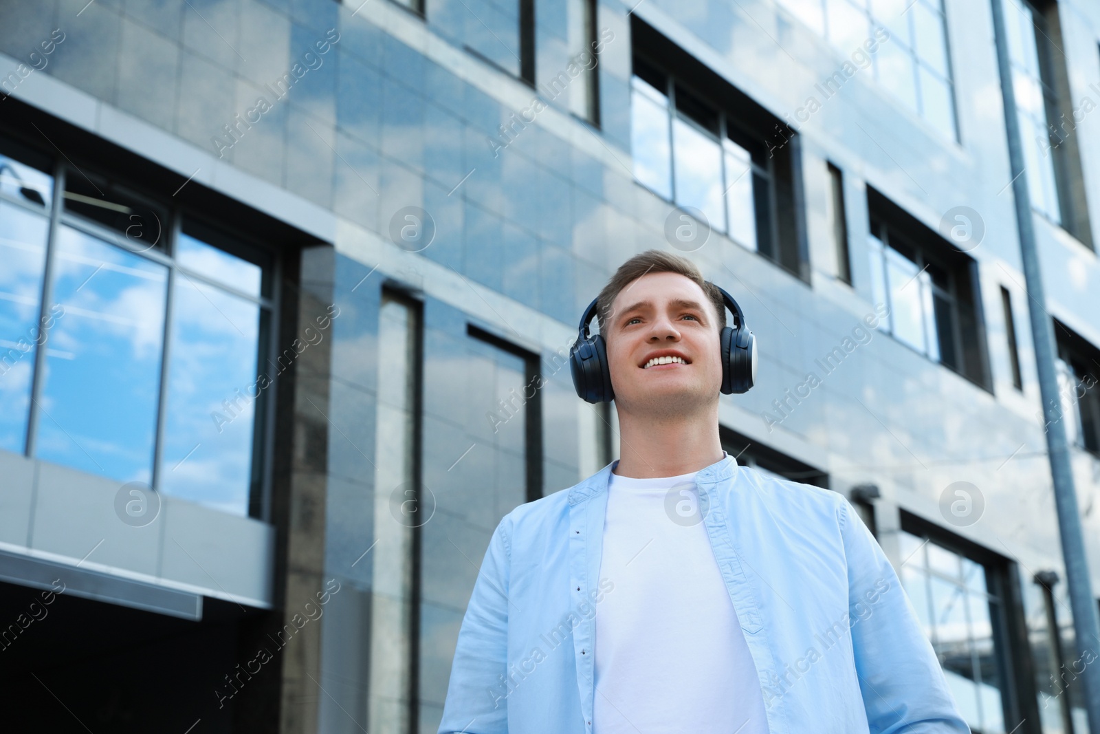 Photo of Smiling man wearing headphones near building outdoors, low angle view. Space for text