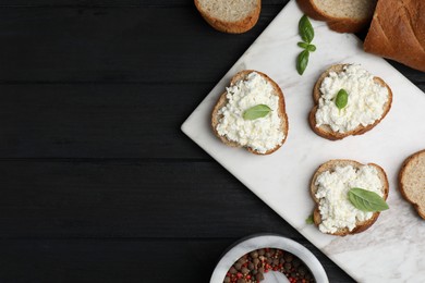 Photo of Bread with cottage cheese and basil on black wooden table, flat lay. Space for text