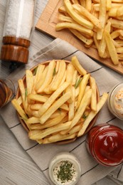 Delicious french fries served with sauces on light wooden table, flat lay