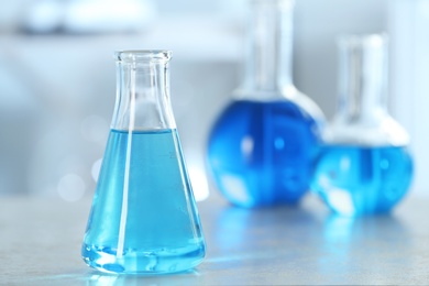 Photo of Conical flask with light blue liquid on table in laboratory. Space for text