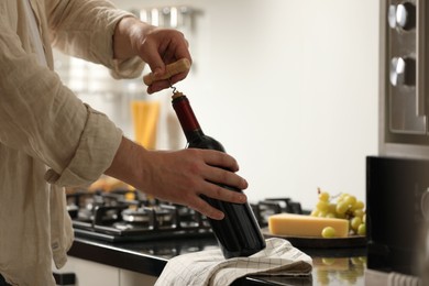 Photo of Man opening wine bottle with corkscrew indoors, closeup. Space for text