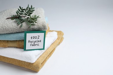 Photo of Recycling concept. Stacked towels and card with plant on white background, space for text