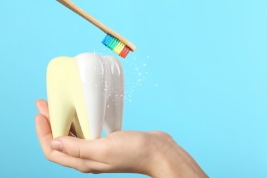 Image of Woman holding ceramic model of tooth and wooden brush on light blue background. Whitening concept
