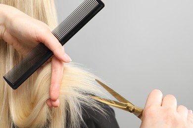 Photo of Hairdresser cutting client's hair with scissors on light grey background, closeup. Space for text