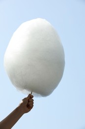 Woman holding white cotton candy against blue sky, closeup