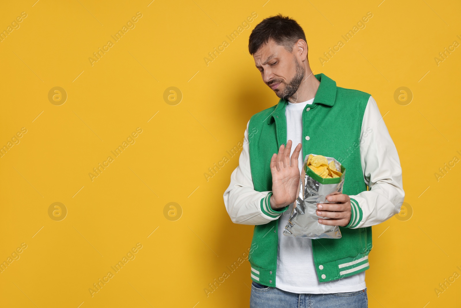 Photo of Handsome man refusing to eat potato chips on orange background, space for text