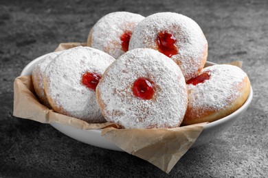 Delicious donuts with jelly and powdered sugar in bowl on grey table