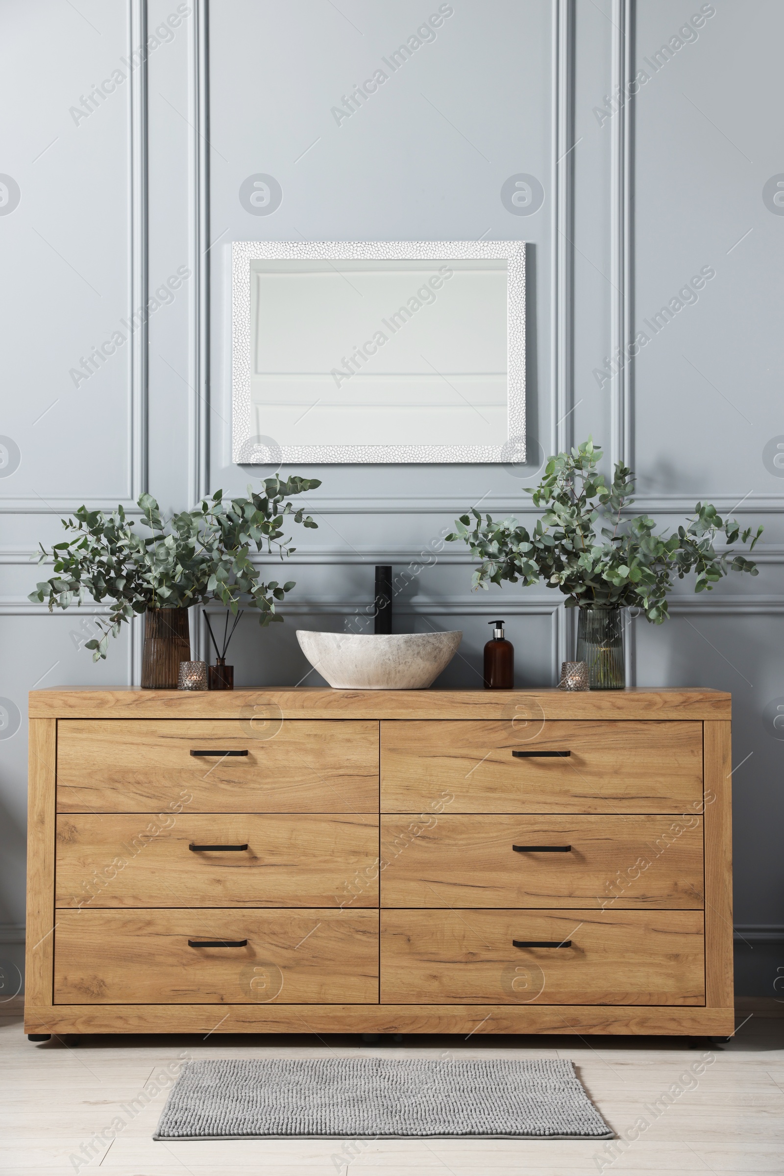 Photo of Modern bathroom interior with stylish mirror, eucalyptus branches, vessel sink and wooden vanity