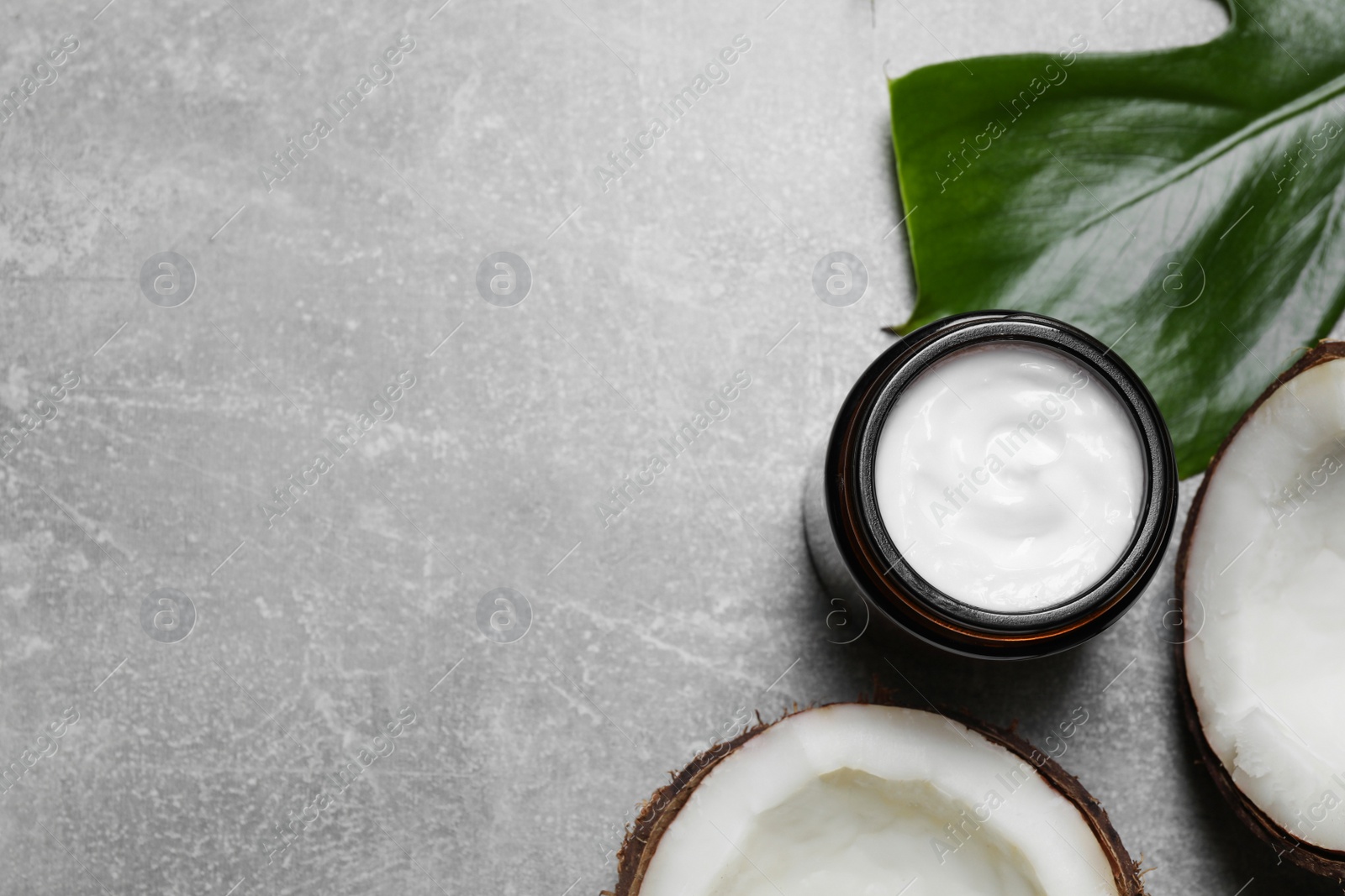 Photo of Jar of hand cream and coconut pieces on grey table, flat lay. Space for text