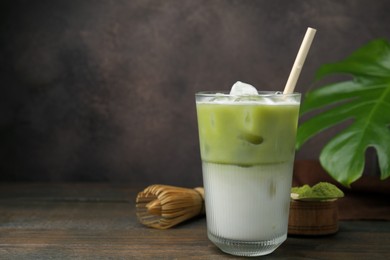 Photo of Glass of tasty iced matcha latte, bamboo whisk and powder on wooden table. Space for text