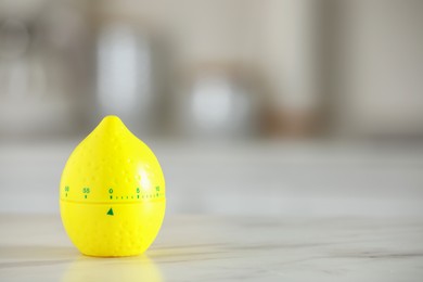 Photo of Kitchen timer in shape of lemon on white marble table against blurred background. Space for text