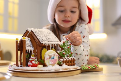 Photo of Cute little girl near gingerbread house indoors