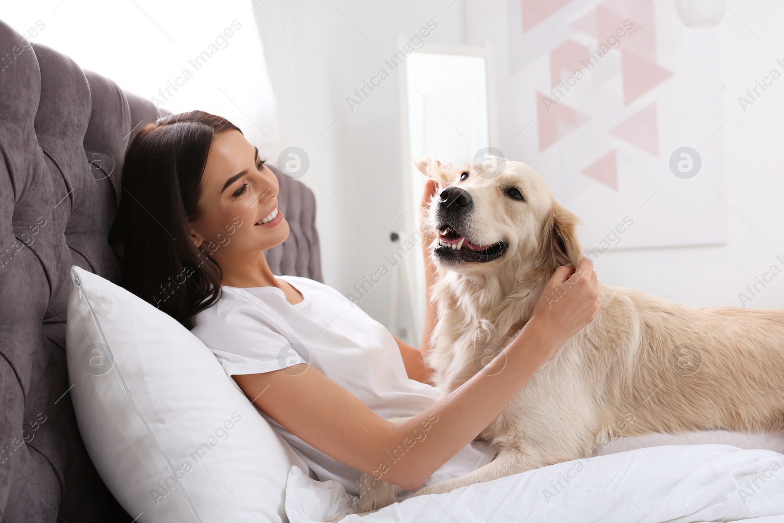 Photo of Young woman and her Golden Retriever dog on bed at home