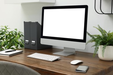 Comfortable workplace at home. Modern computer with blank screen and houseplants on wooden desk. Mockup for design