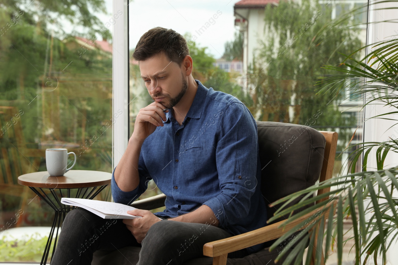 Photo of Man solving sudoku puzzle in armchair at home