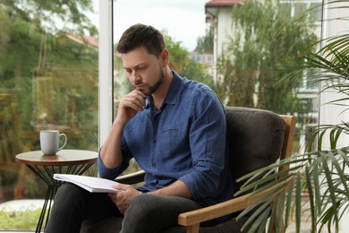 Photo of Man solving sudoku puzzle in armchair at home