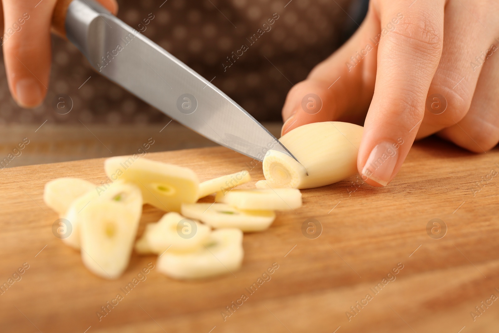 Photo of Woman cutting fresh garlic at wooden table, selective focus
