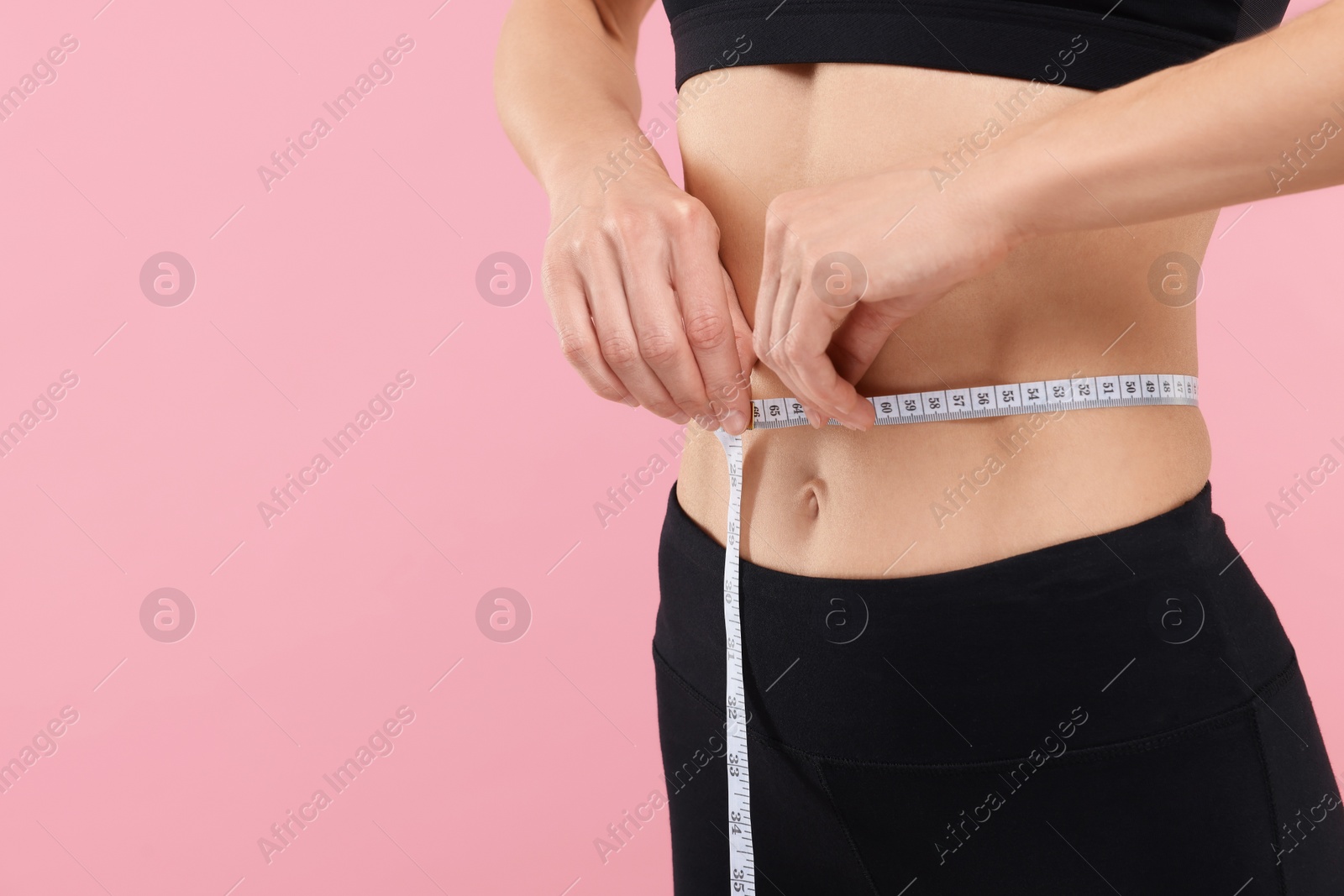 Photo of Slim woman measuring waist with tape on pink background, closeup and space for text. Weight loss