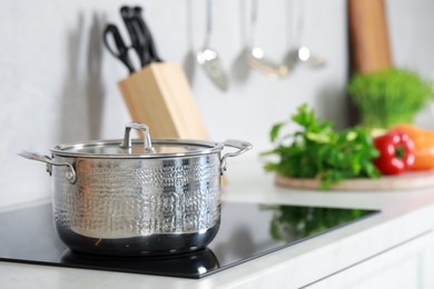 Pot with lid on cooktop in kitchen, space for text. Cooking utensils