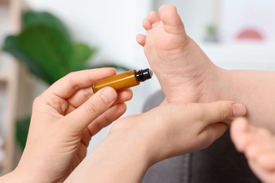 Mother applying essential oil from roller bottle onto her baby`s heel indoors, closeup