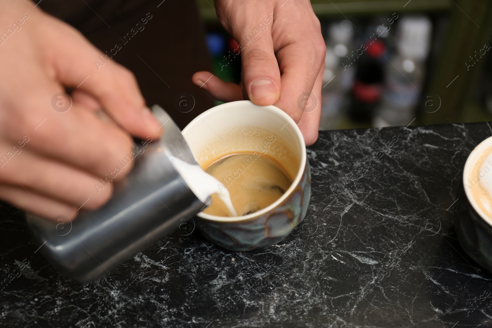 Photo of Barista adding milk to coffee at table, closeup