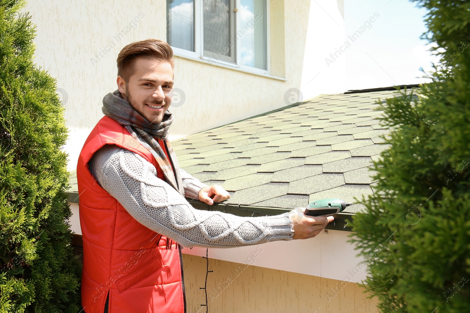 Photo of Young man decorating roof with Christmas lights