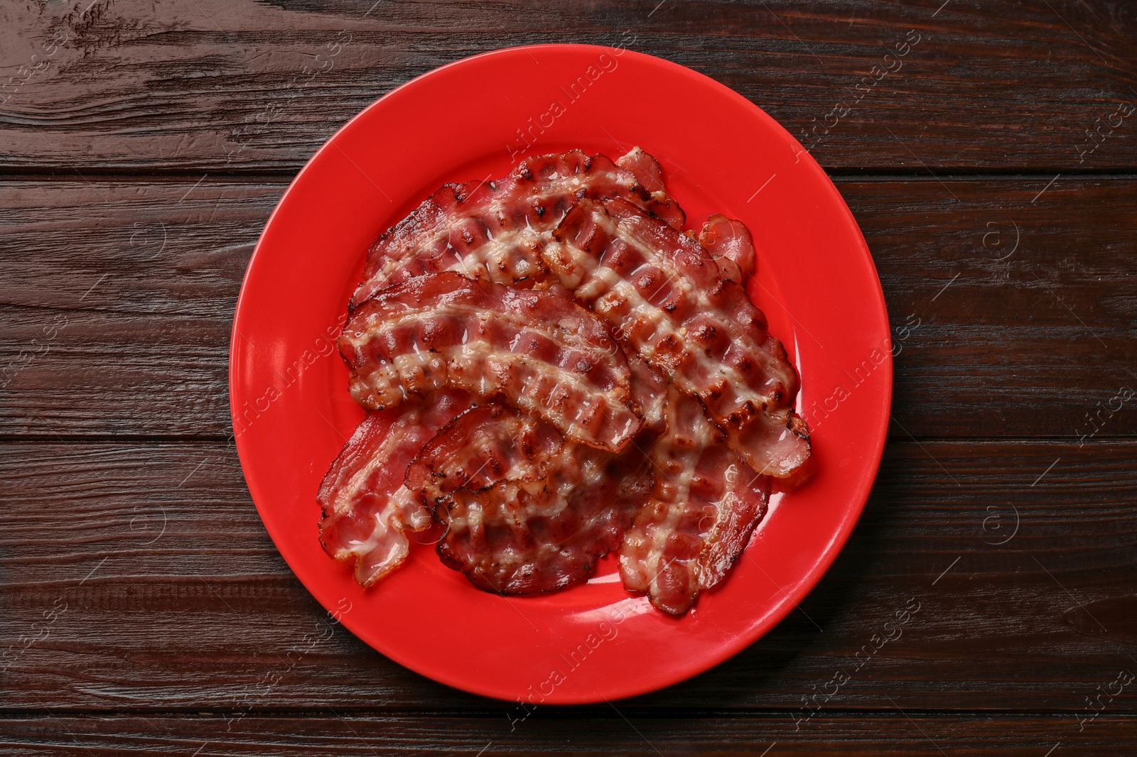 Photo of Plate with fried bacon slices on wooden table, top view