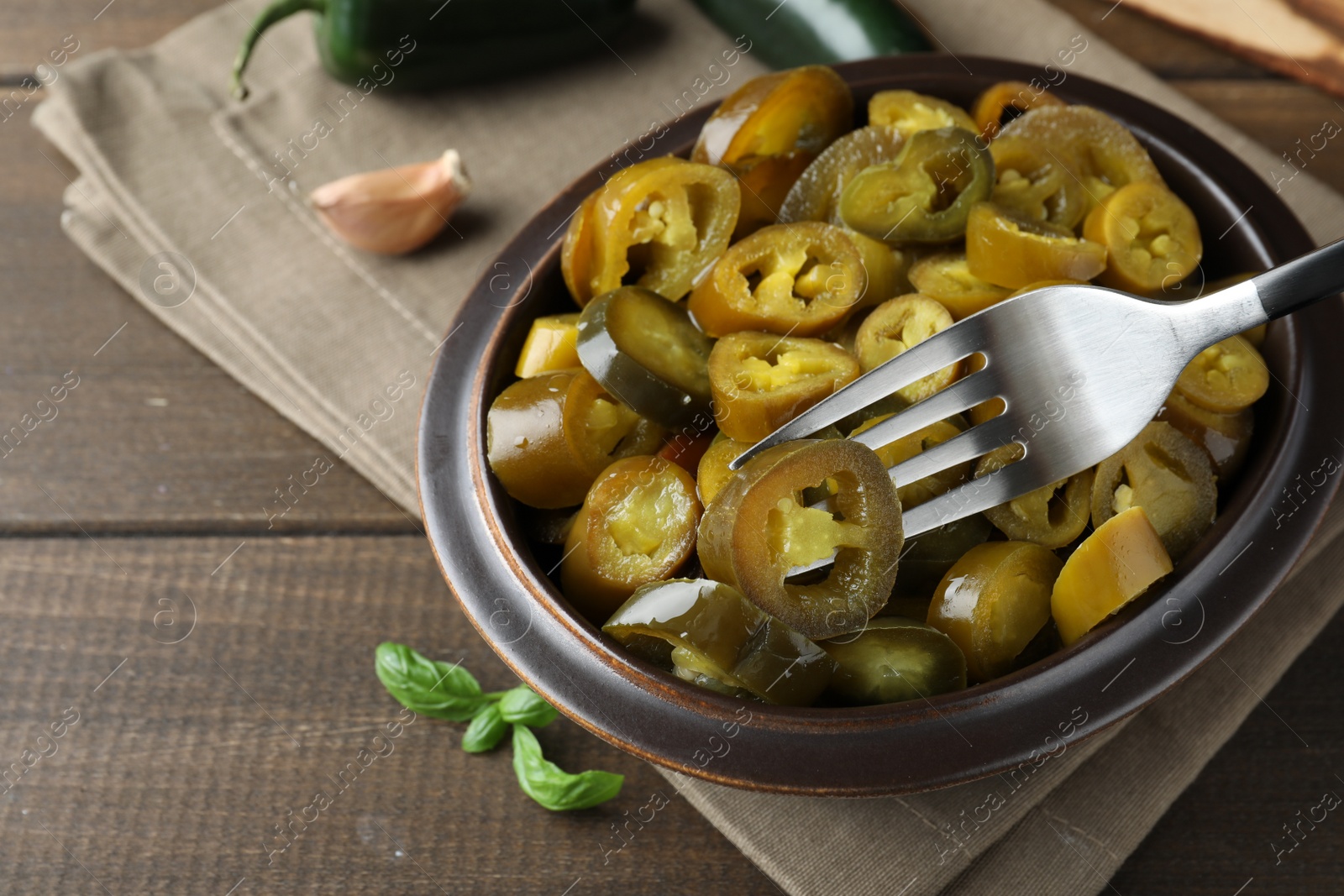 Photo of Taking slice of pickled green jalapeno with fork from bowl on wooden table
