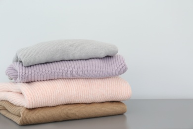 Stack of folded warm knitted sweaters on grey table