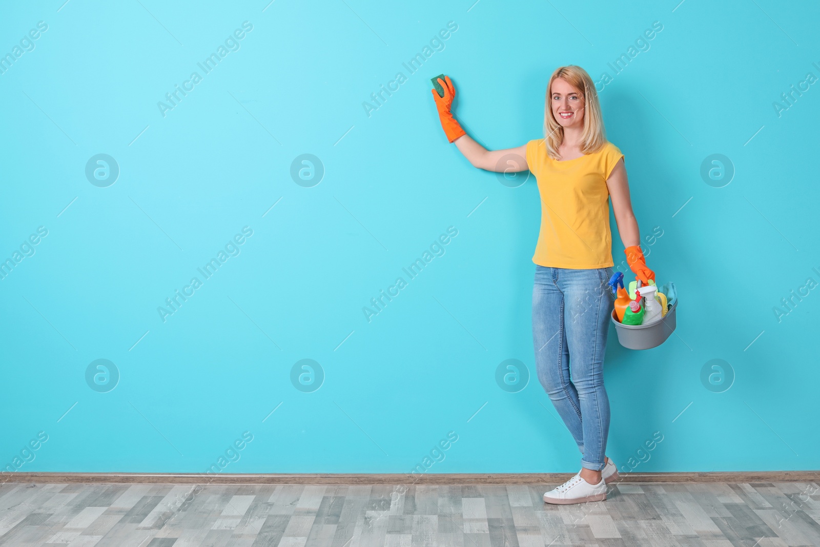 Photo of Woman in gloves cleaning color wall with sponge