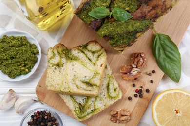 Freshly baked pesto bread with ingredients on white wooden table, flat lay