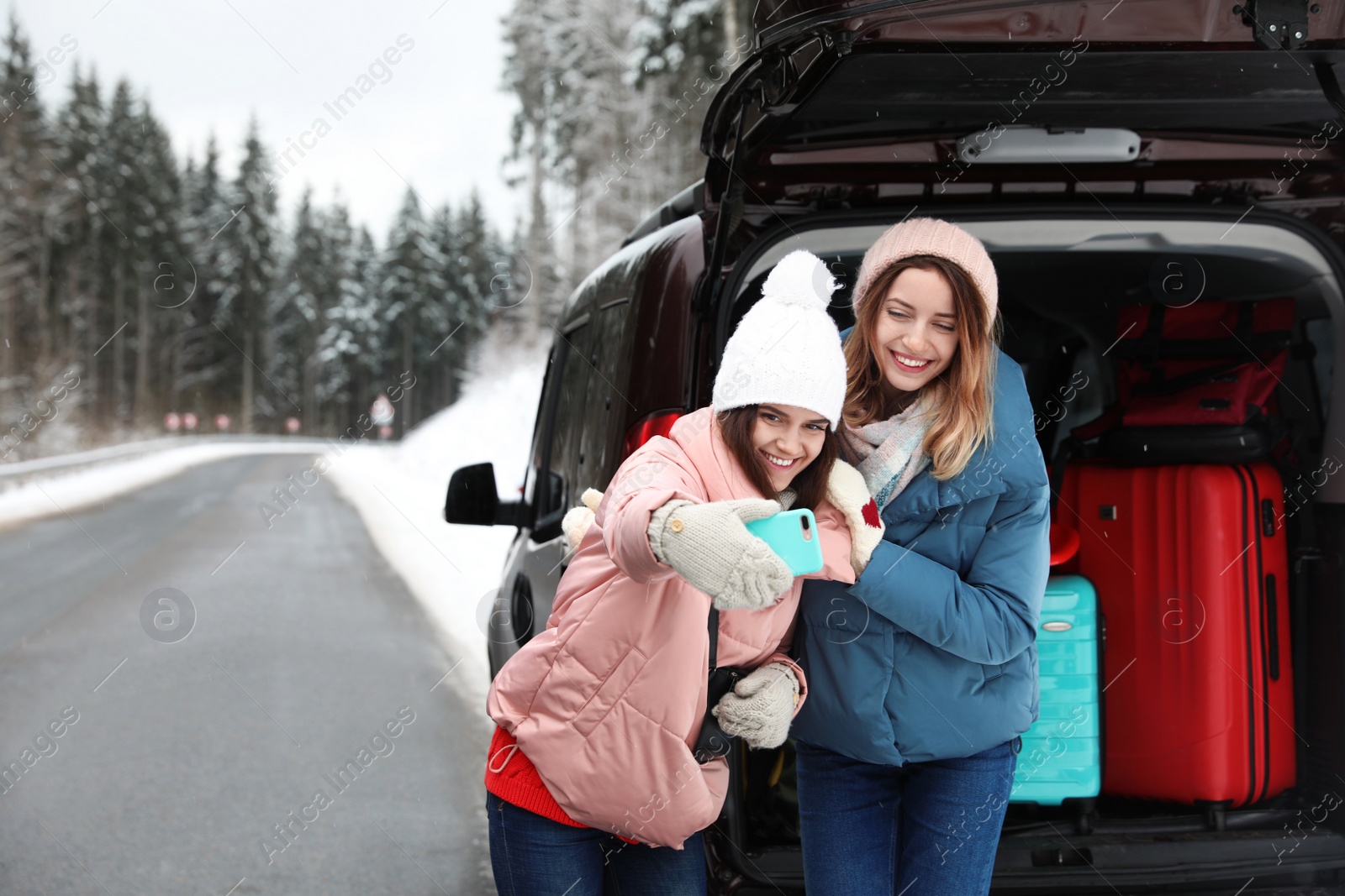 Photo of Friends taking selfie near open car trunk full of luggage on road, space for text. Winter vacation