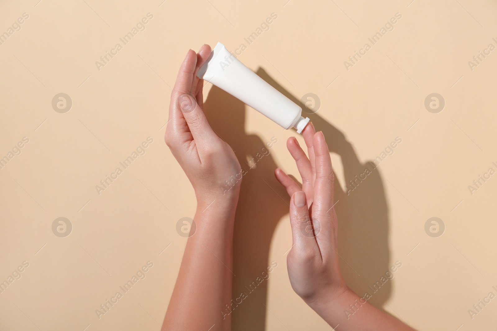 Photo of Woman with tube of hand cream on beige background, top view