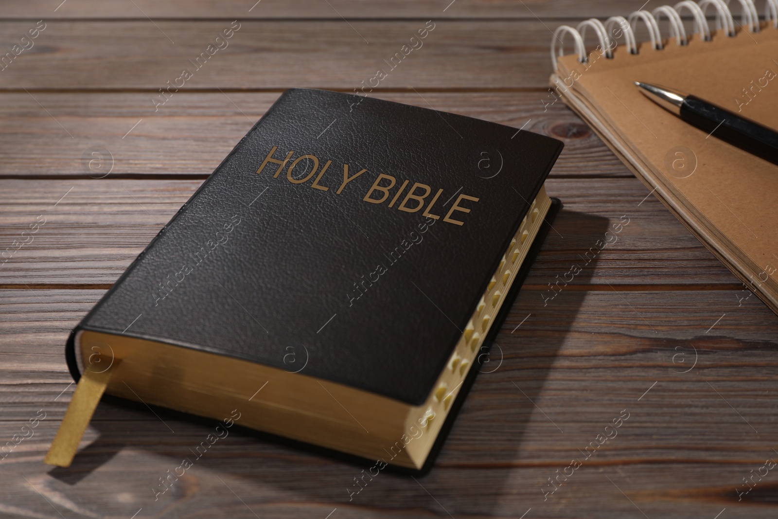 Photo of Old hardcover Bible and notebook with pen on wooden table. Religious book