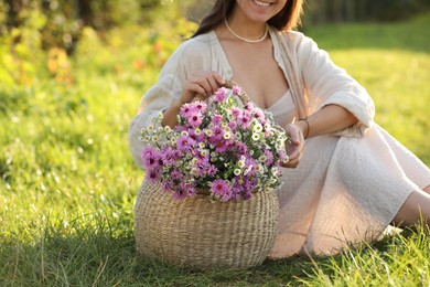 Photo of Woman holding wicker basket with beautiful wild flowers outdoors, closeup