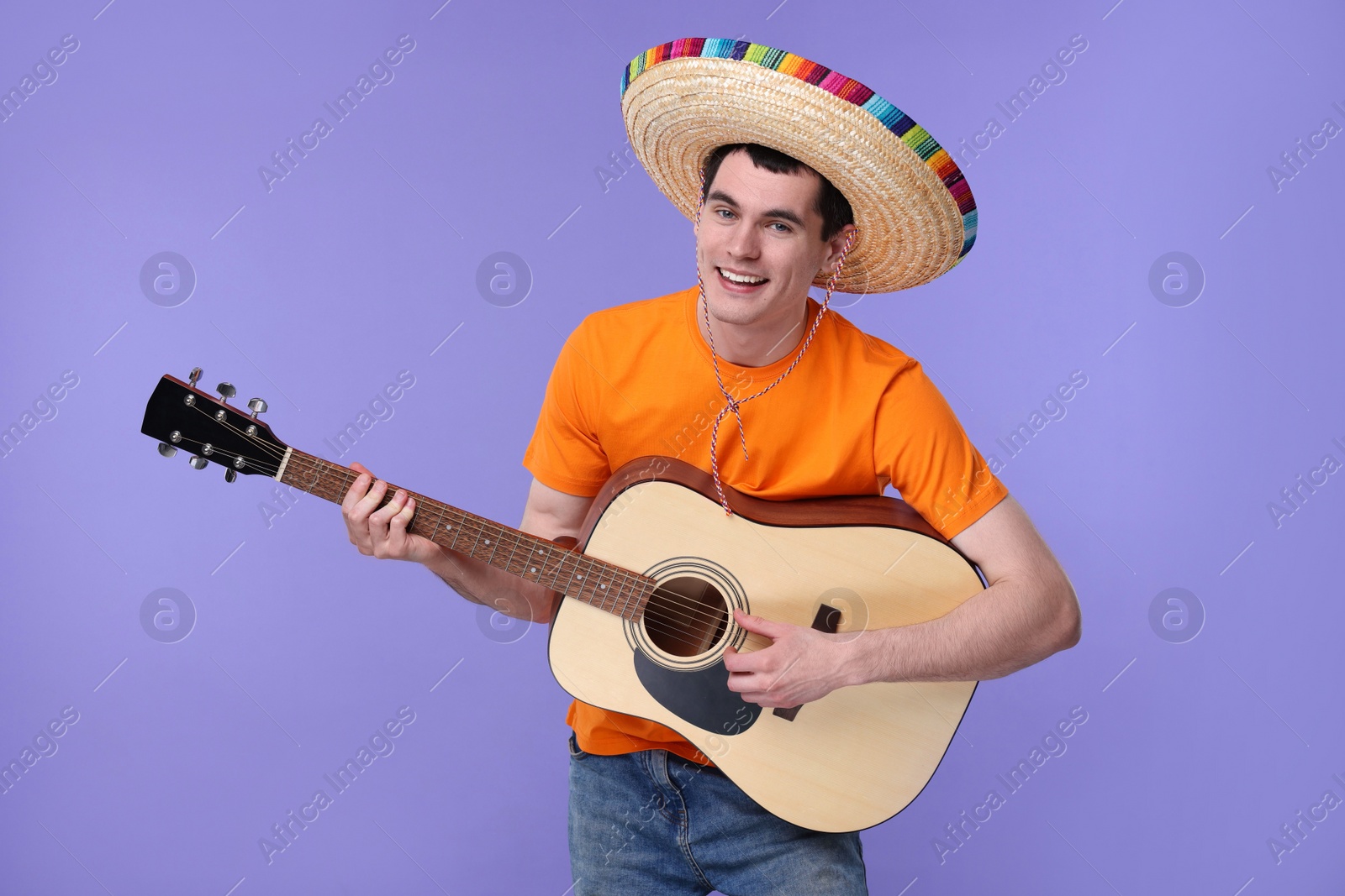 Photo of Young man in Mexican sombrero hat playing guitar on violet background