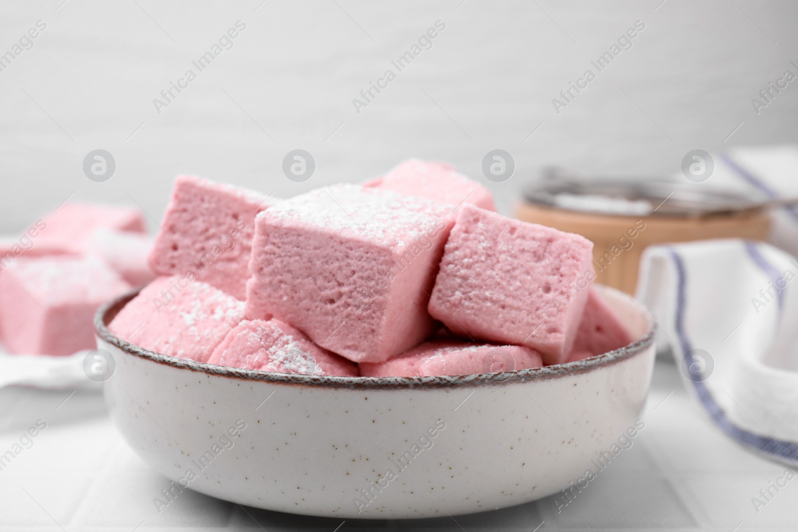 Photo of Bowl of delicious sweet marshmallows with powdered sugar on white table, closeup