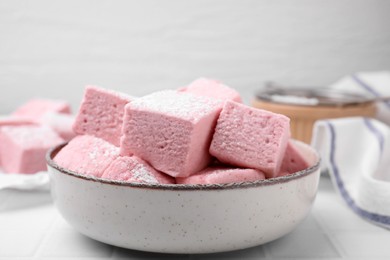 Bowl of delicious sweet marshmallows with powdered sugar on white table, closeup