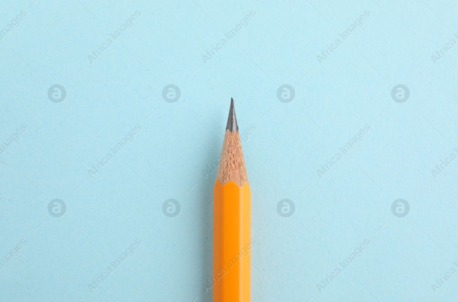 Photo of One sharp graphite pencil on light blue background, top view