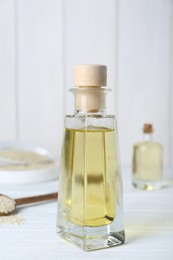 Glass bottle of sesame oil and seeds on white wooden table