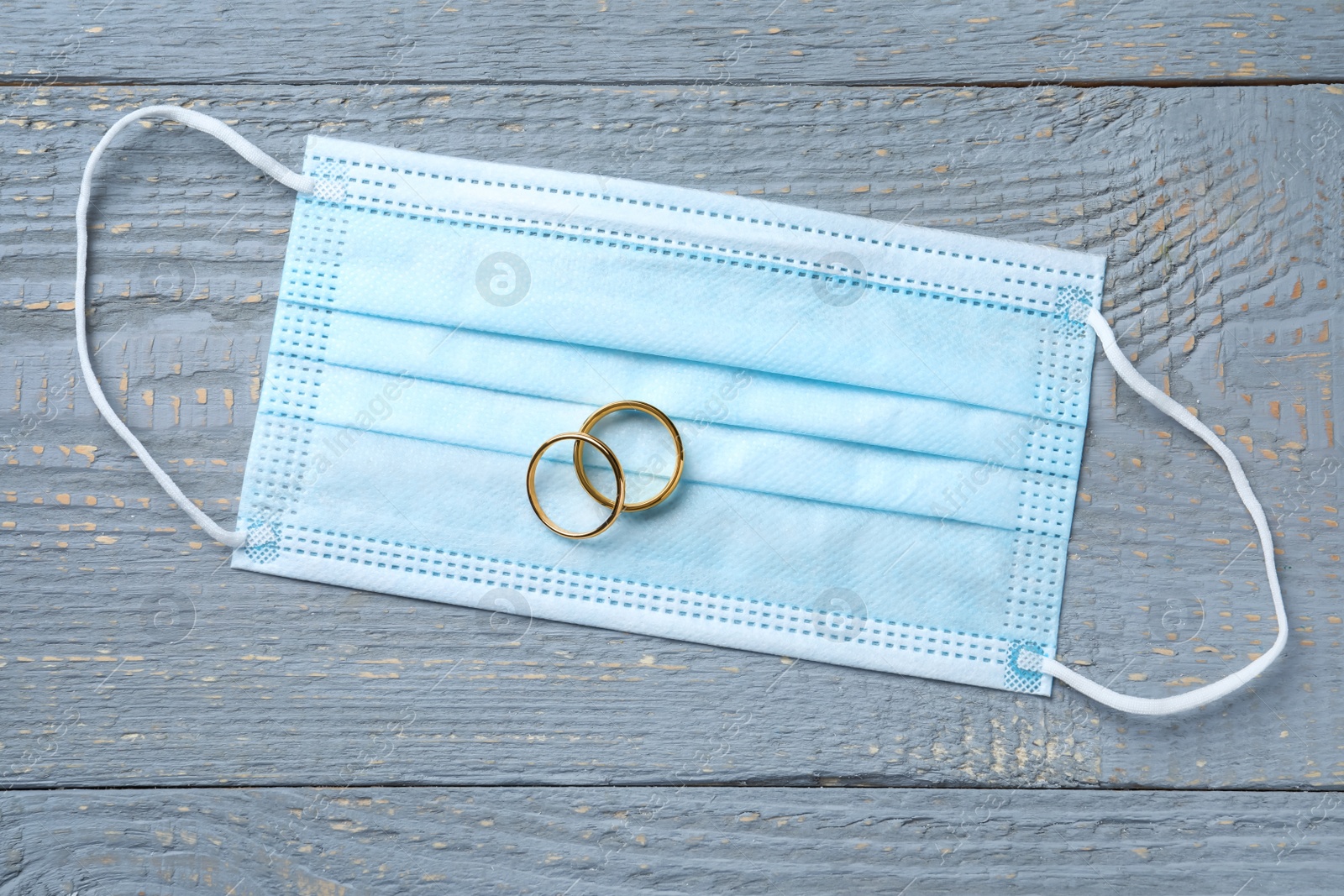 Photo of Protective mask and wedding rings on grey wooden table, flat lay. Divorce during coronavirus quarantine