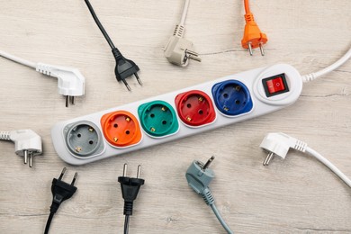 Power strip with extension cord on white wooden floor, flat lay. Electrician's equipment