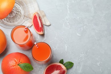 Photo of Tasty freshly made grapefruit juice and fruits on light grey marble table, flat lay. Space for text